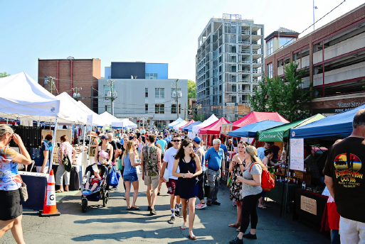 People line the street path of the Charlottesville City Market. Vendor stalls line both sides of the street.