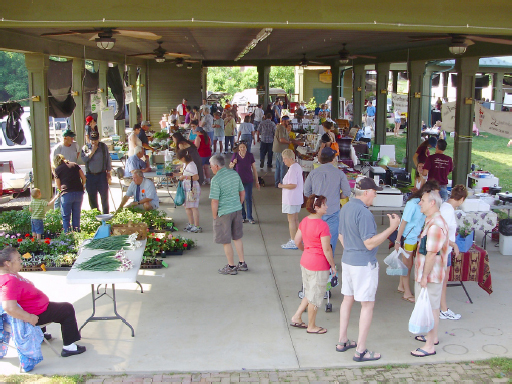 A large crowd stands underneath the pavilion, chatting and looking at the products.