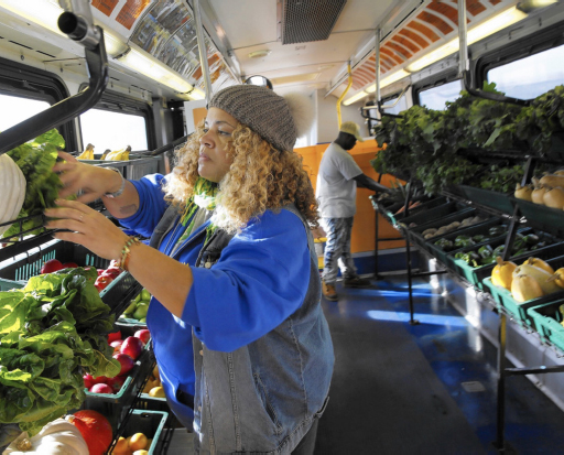 A lady is picking produce from one of the rows of produce baskets that have been installed inside the converted Fresh Moves Mobile Market Bus.